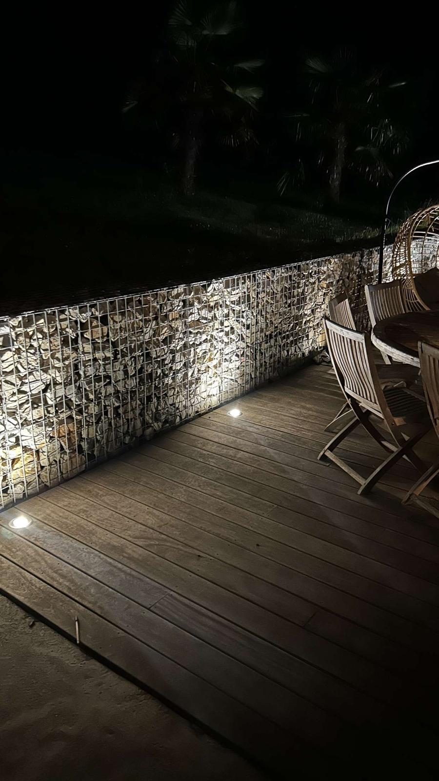Muret gabion éclairé le long d'une terrasse bois de nuit